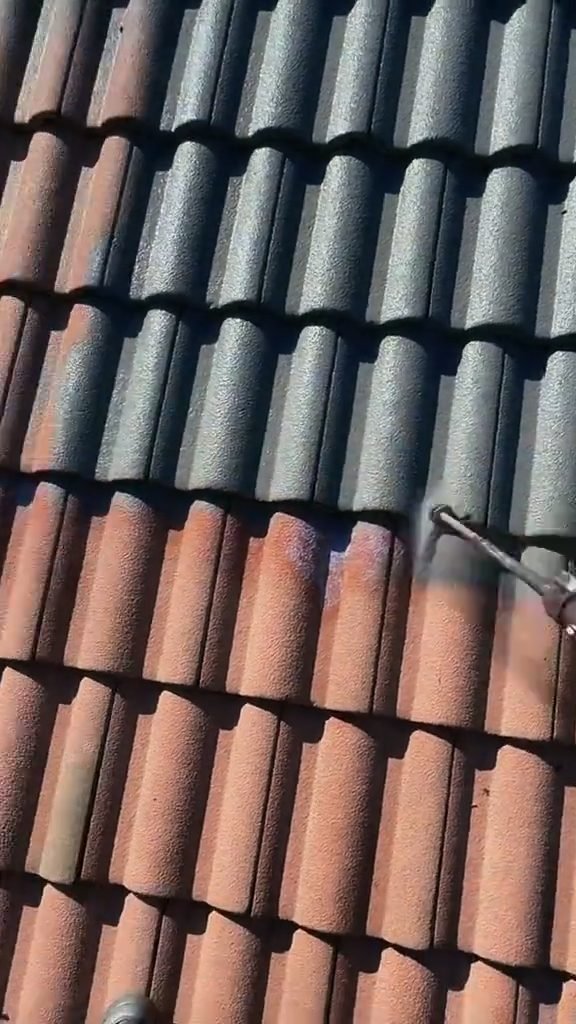 A spray gun laying a dark coat over terracotta roof tiles