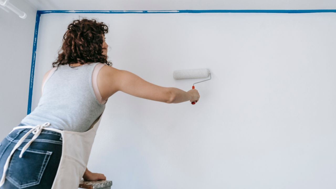 Painter rolling white paint onto a wall edged with blue masking tape