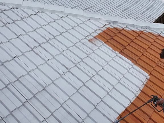 Roof tiles being sprayed with white primer, the terracotta still to do beside them