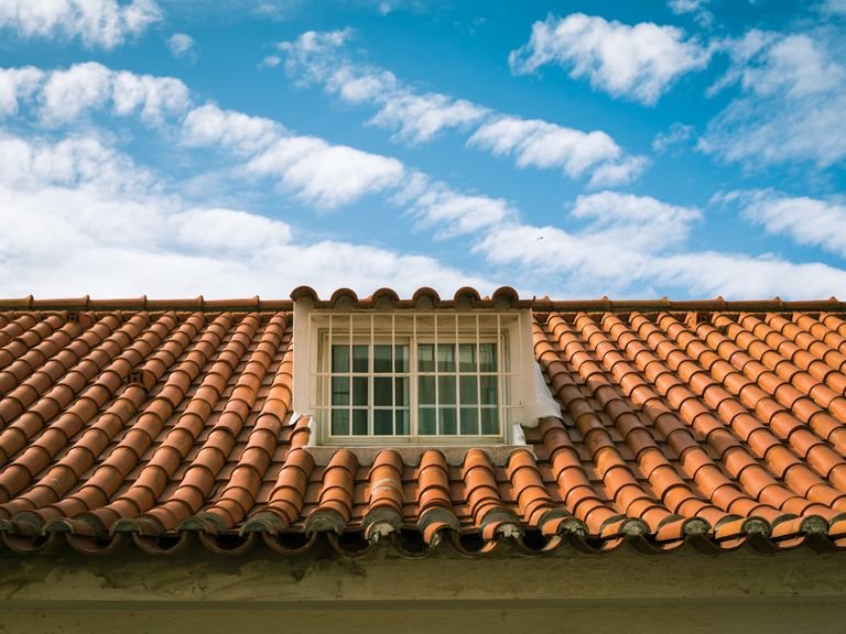 Orange tiled roof with a white dormer window under a cloudy sky
