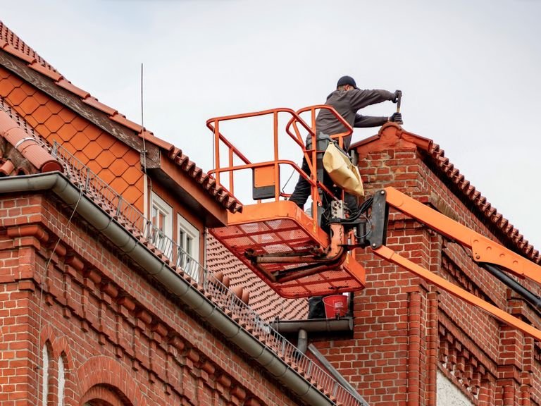 Roofer on an access platform working at the top of a brick gable